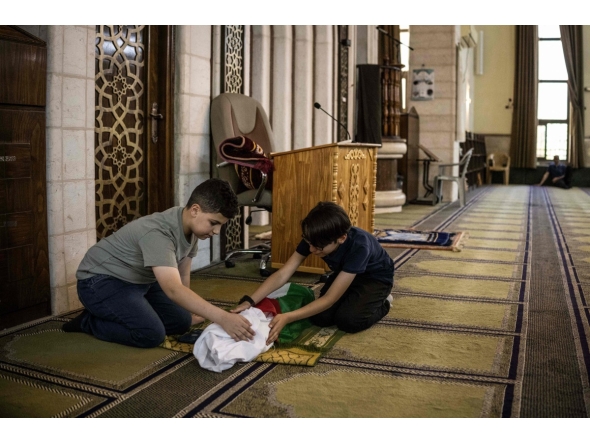 This photo taken on June 6, 2026 shows Kinan Abou Haikal (L), the elder brother of seven-month-old baby Sam Fahd Abou Haikal, sitting next to his body at the Abou Heisheh Mosque in Hebron, in the Israeli-occupied West Bank. (Photo by JOHN WESSELS / AFP)