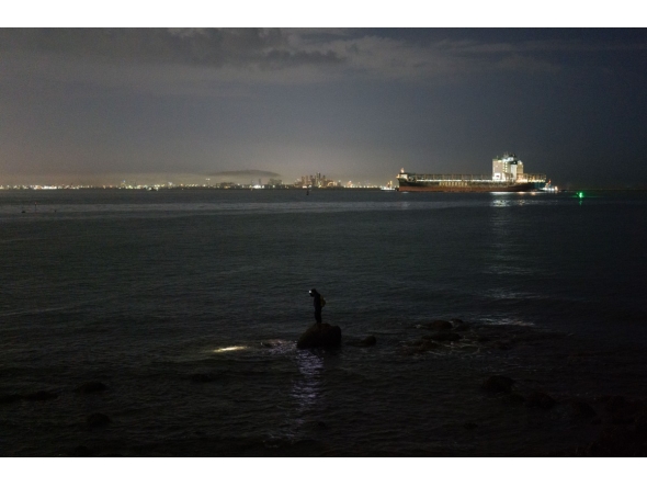 An angler (C) uses a headlamp before casting his line, as a large cargo container ship sails towards the Laem Chabang Port, near the city of Pattaya on September 1, 2026. (Photo by ANTHONY WALLACE / AFP)
