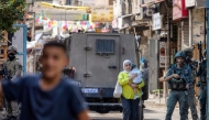 A Palestinian woman carrying a child walks past members of the Israeli occupation army and armoured vehicles during an Israeli military operation at the Balata camp for Palestinian refugees, east of Nablus in the occupied West Bank, on August 31, 2026. Photo by JAAFAR ASHTIYEH / AFP