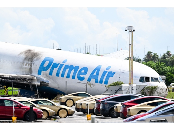 A parking lot filled with Tesla Cybercabs is seen in the foreground as the nose of a Prime Air cargo plane rests on the ground after the aircraft overran the runway and struck cars the previous day at Miami International Airport in Miami, Florida, on September 7, 2026. (Photo by CHANDAN KHANNA / AFP)