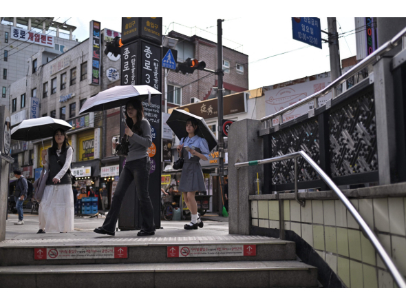 People shield themselves with umbrellas while walking past the metro station entrance in Jongno 3-ga in Seoul on September 20, 2026. (Photo by Lillian SUWANRUMPHA / AFP)