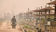 A worker pushes a wheelbarrow through a public cemetery blanketed in thick smoke haze caused by forest and land fires in Palangka Raya, Central Kalimantan province on September 30, 2026. (Photo by REINA / AFP)