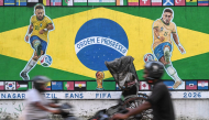Motorcyclists ride past a graffiti featuring Brazilian football player Neymar (L) and Raphinha ahead of a FIFA international friendly football match between India and Brazil in Kolkata on September 29, 2026. (Photo by Dibyangshu Sarkar / AFP)
