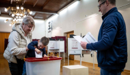 A child accompanied by his parents casts a ballot at a polling station during Latvia's parliamentary elections in Riga on October 3, 2026. (Photo by Wojtek Radwanski / AFP)