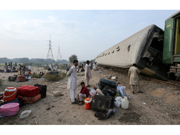  Passengers sit with their belongings next to derailed coaches of the passenger train Rehman Baba Express on the outskirts of Multan on October 13, 2026. (Photo by Shahid Saeed MIRZA / AFP)