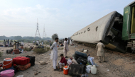  Passengers sit with their belongings next to derailed coaches of the passenger train Rehman Baba Express on the outskirts of Multan on October 13, 2026. (Photo by Shahid Saeed MIRZA / AFP)