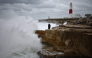 Members of the public stand on rocks as waves break near Portland Bill Lighthouse in Portland, southern England on October 23, 2026, as Storm Austen brings strong winds and heavy rain across much of southern England. (Photo by Henry Nicholls / AFP)