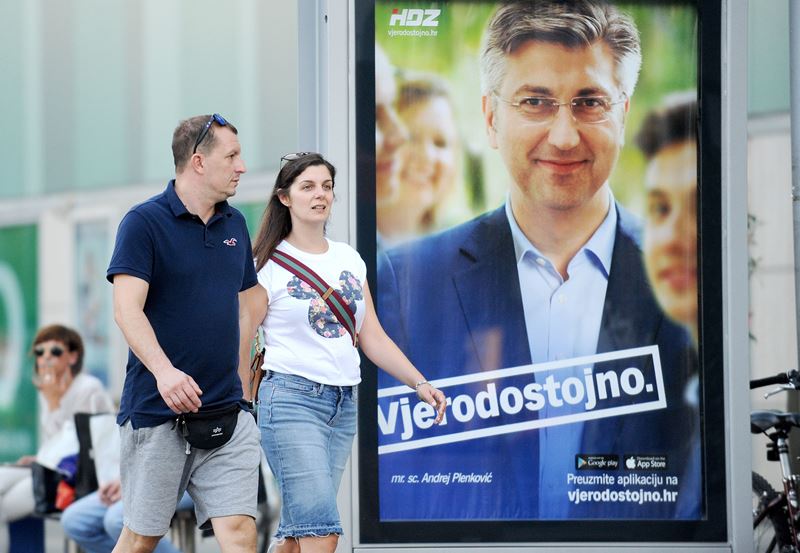 People pass a campaign poster of Chief of the conservative HDZ party Andrej Plenkovic waves in Zagreb on September 8, 2016. Croatians will choose between two career diplomats for their next prime minister on September 11's early election, which follows mo
