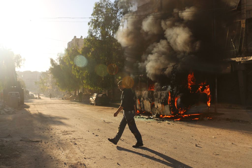  A Syrian man walks past a bus set ablaze following a reported air strike in the rebel-held Salaheddin district of Aleppo on September 25, 2016. The UN Security Council met for urgent talks as Syrian and Russian warplanes pounded rebel-held east Aleppo in