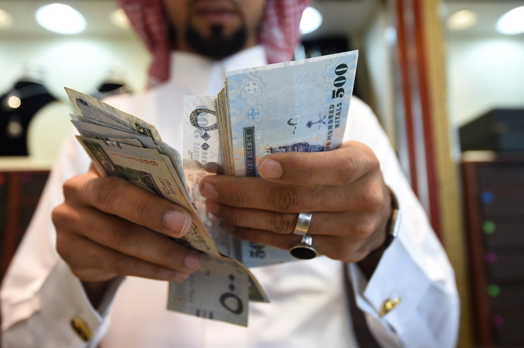 A man counts Saudi riyal banknotes at his jewelry shop in Tiba market in the capital Riyadh on October 3, 2016. / AFP / FAYEZ NURELDINE