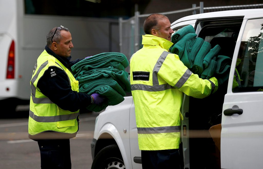 Border force officials carry blankets used by child migrants as they were brought by coach from 