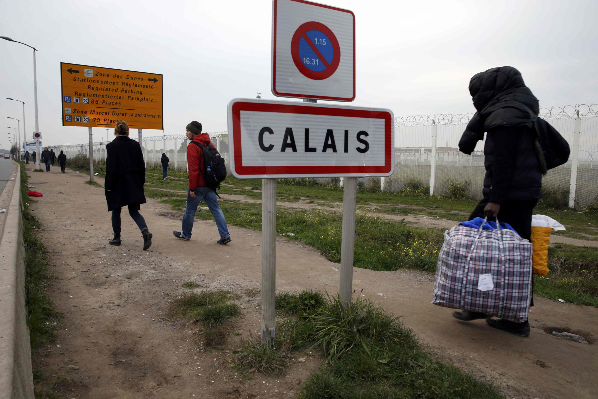 A migrant carries bags with his belongings as he walks past the Calais city limit sign on the eve of the evacuation and transfer of migrants to reception centers in France, and the dismantlement of the camp called the 