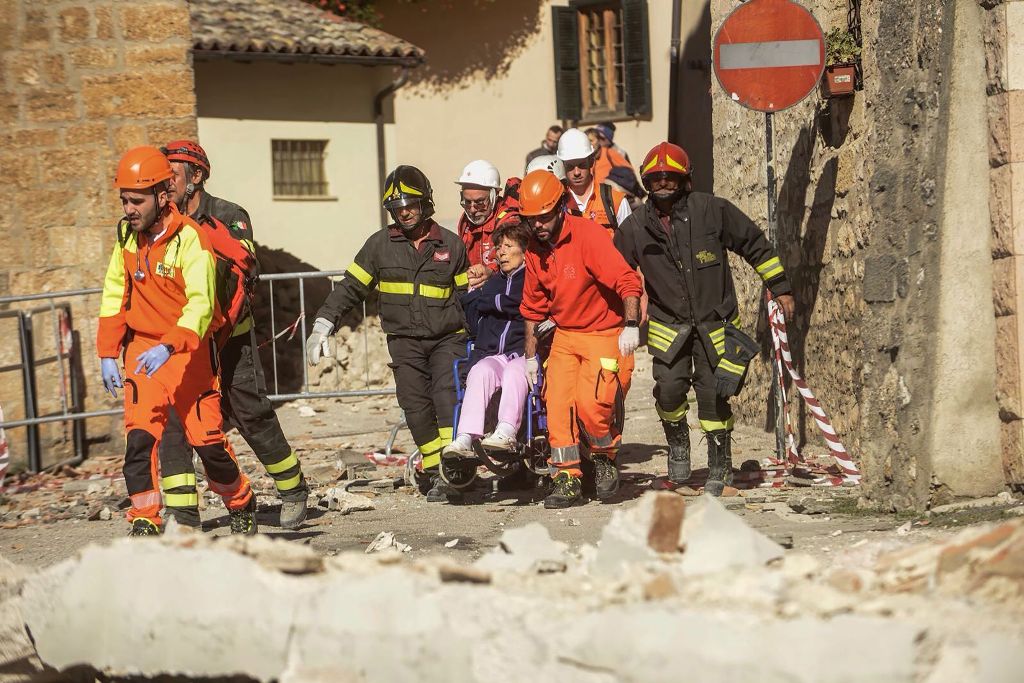 Firefighters and rescuers carry a woman on a wheelchair after a 6.6 magnitude earthquake on October 30, 2016 in Norcia. / AFP / Fabrizio Troccoli.