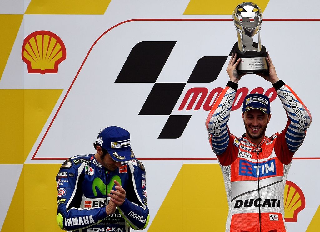 Second-placed Movistar Yamaha MotoGP's Italian rider Valentino Rossi (L) looks on as Ducati Team's Italian rider Andrea Dovizioso (R) holds up the winner's trophy as they celebrate on the podium after the 2016 Malaysian MotoGP at the Sepang International 