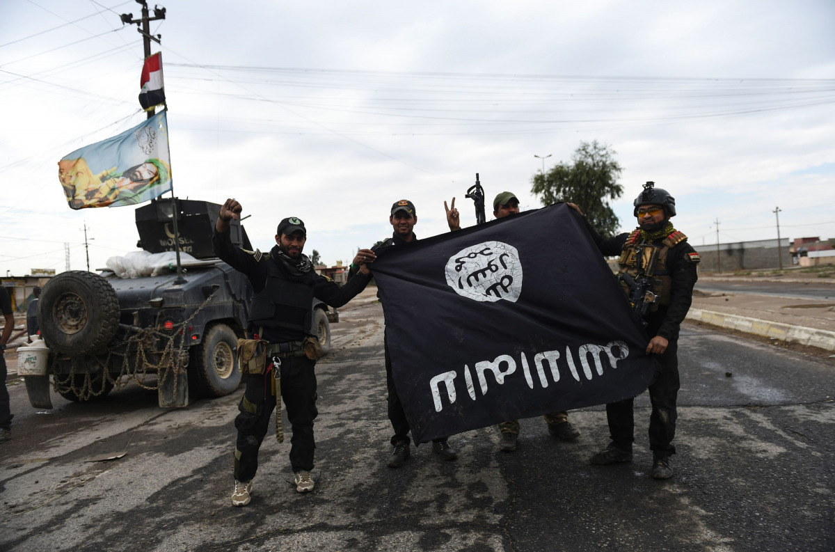 Iraqi soldiers pose with an Islamic State (IS) group flag as they hold a position in the village of Gogjali, a few hundred metres of Mosul's eastern edge, on November 2, 2016, as clashes go on between Iraqi army forces and the jihadists to retake Mosul, t