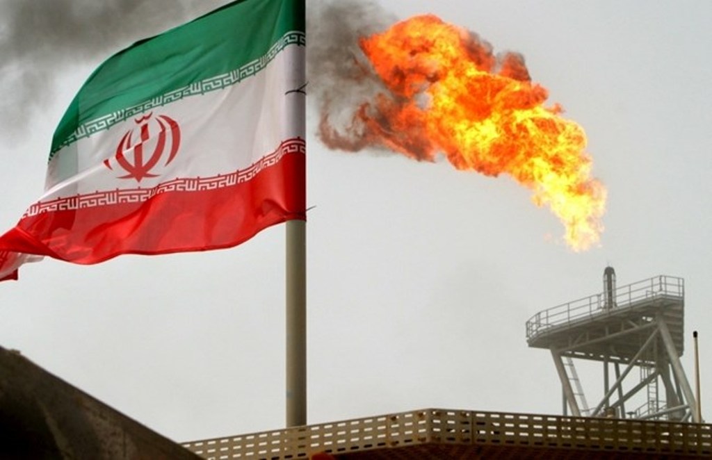 A gas flare on an oil production platform in the Soroush oil fields is seen alongside an Iranian flag in the Persian Gulf, Iran, July 25, 2005. REUTERS/Raheb Homavandi/File Photo.