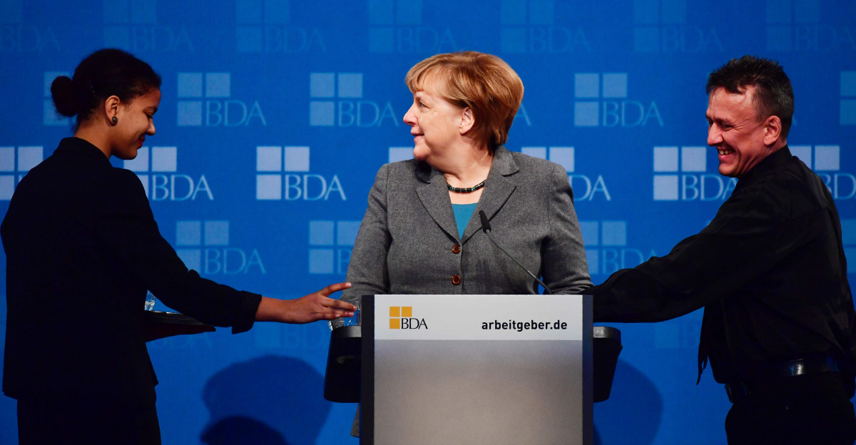 German Chancellor Angela Merkel (C) smiles as two waiters attend to her before starting her speech at a meeting of the Confederation of German Employers' Associations (BDA - Bundesvereinigung der Deutsche Arbeitgaeberverbaende) in Berlin on November 15, 2