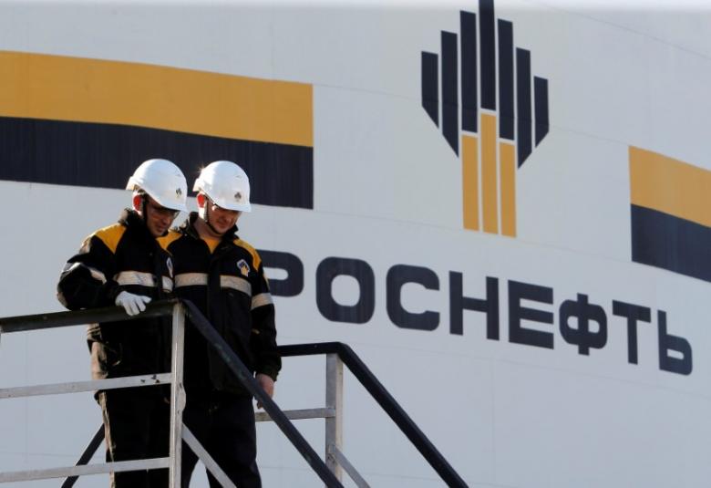 Workers stand next to a logo of Russia's Rosneft oil company at the central processing facility
