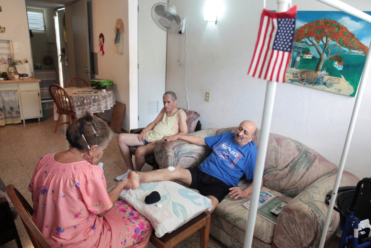 Juanita Gomez Cruz (L) cleans her husband Pedro after he suffered a foot amputation several years ago as their son Dafner sits next to them at their home, in San Juan, Puerto Rico, November 15, 2016. Picture taken November 15, 2016. REUTERS/Alvin Baez