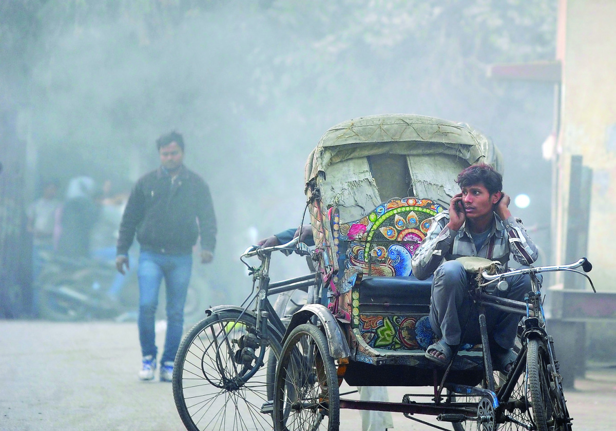 A rickshaw puller talks on his mobile phone as smoke emanates from garbage burning on a road in Allahabad, yesterday. 
