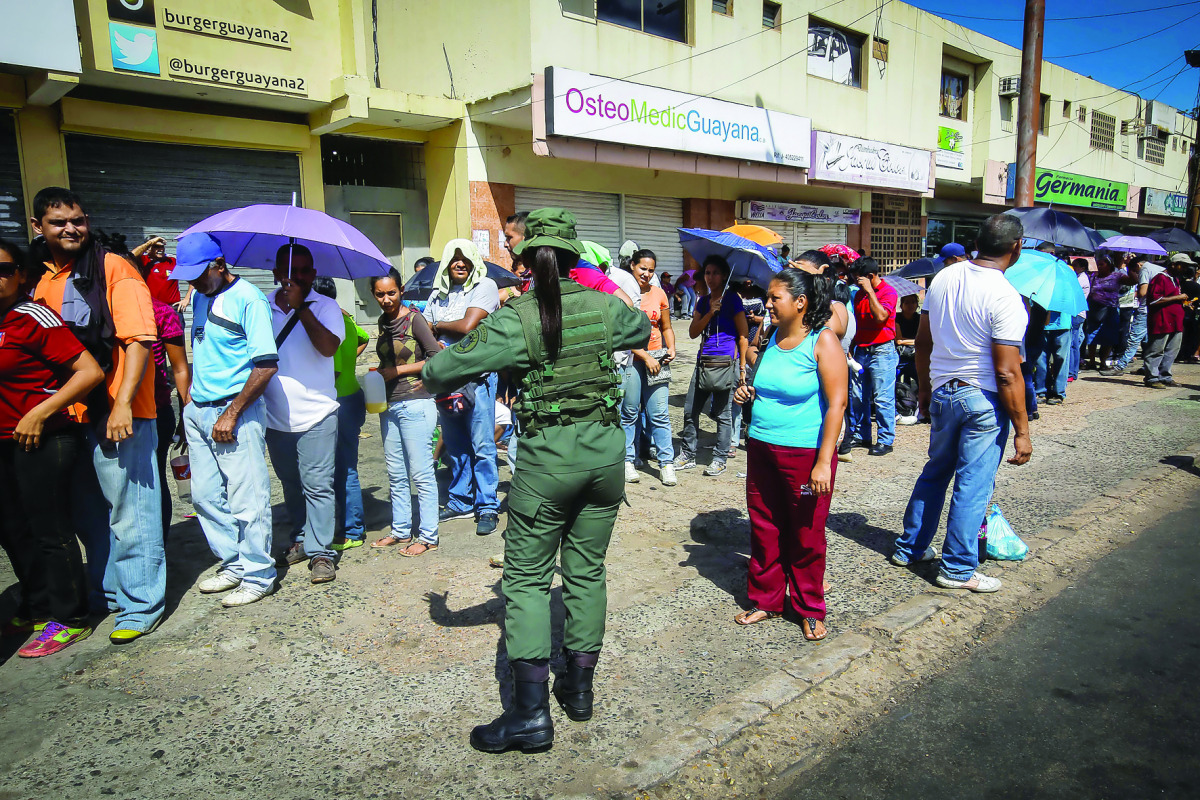 A Venezuelan soldier controls the crowd as people queue to buy goods from a food wholesaler in Ciudad Bolivar, yesterday.