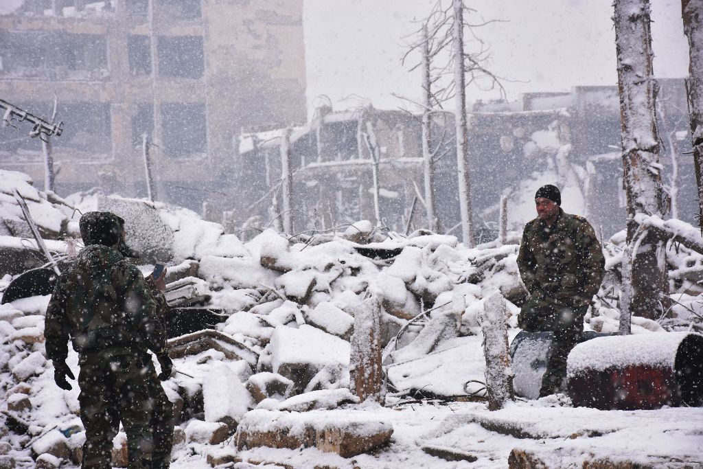 Syrian pro-government forces walk as snow falls in Aleppo on December 21, 2016. The last residents hoping to leave rebel-held Aleppo waited in the snow as delays hit an evacuation that will leave Syria's army in full control of the devastated city. AFP / 