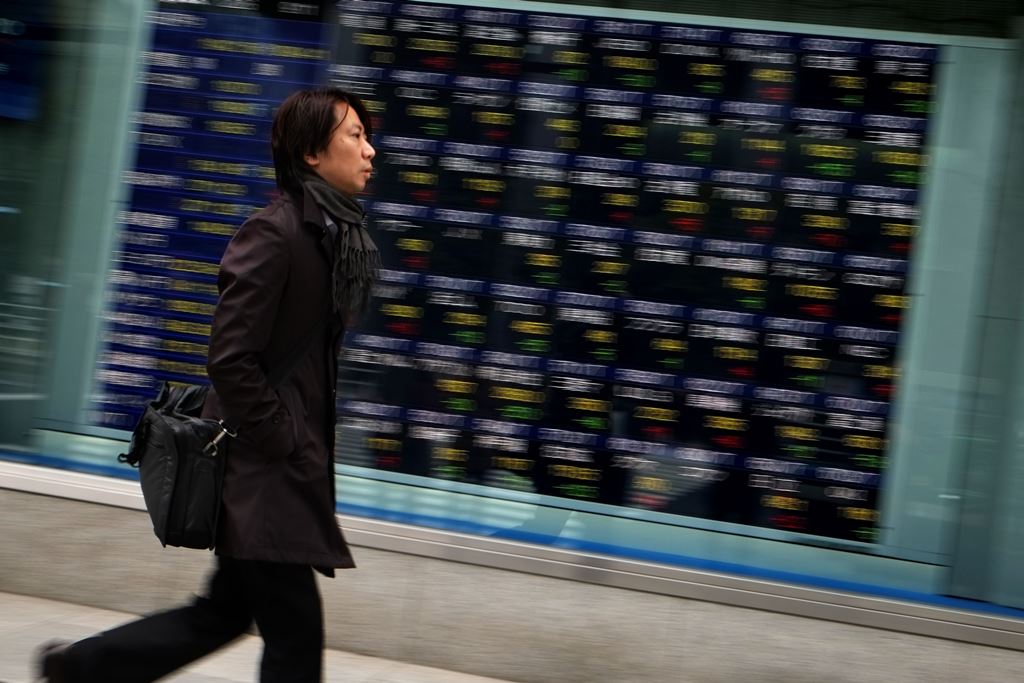 A pedestrian walks past an electronic board displaying stock prices on the Tokyo Stock Exchange in Tokyo on December 26, 2016. AFP / KAZUHIRO NOGI
