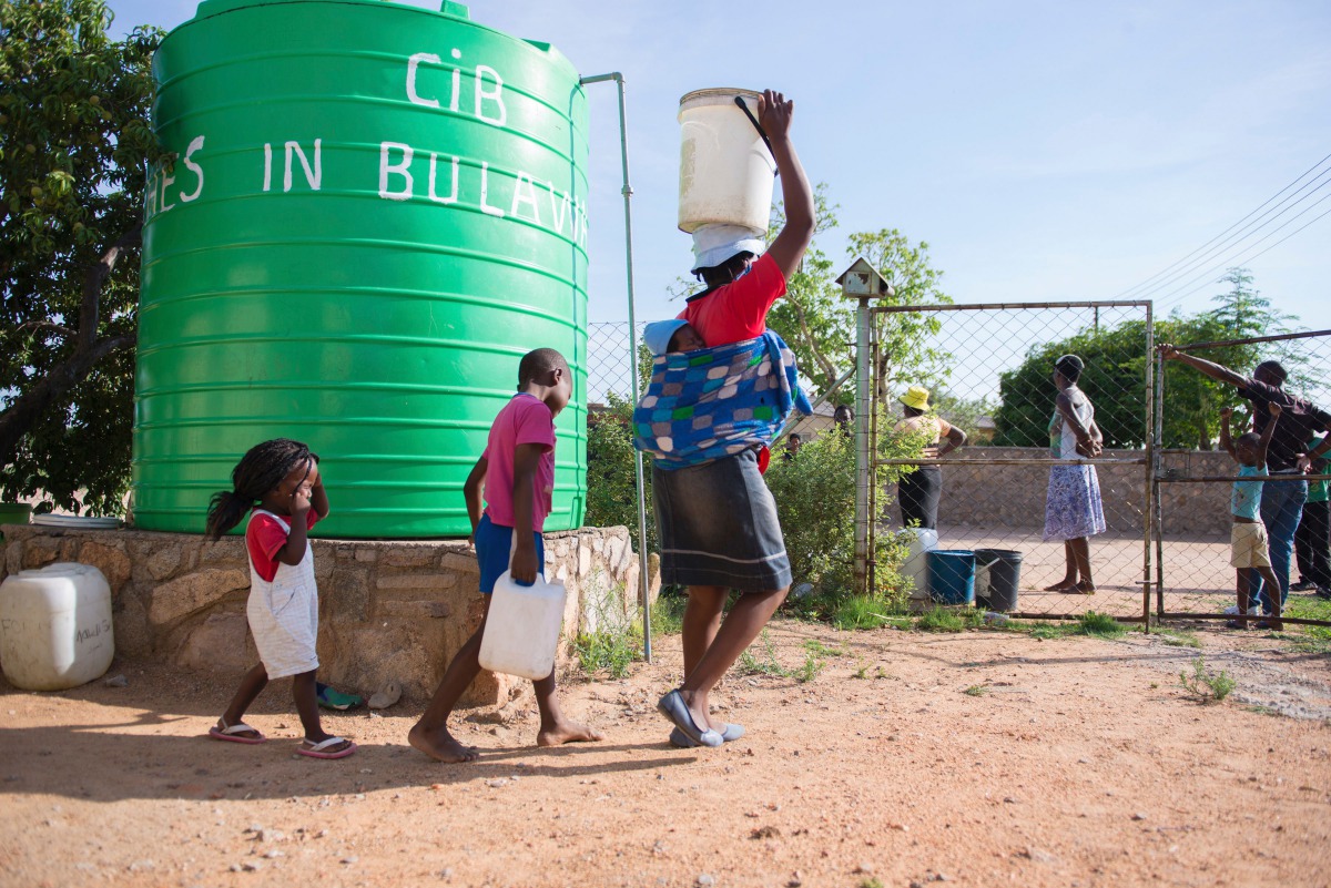 This file photo taken on November 24, 2016 shows a woman and her children carrying water cans, fetched from a tank installed at a church in Luveve on the outskirts of Bulawayo, Zimbabwe. From jobless youths hired to dig wells to illegal sellers supplying 