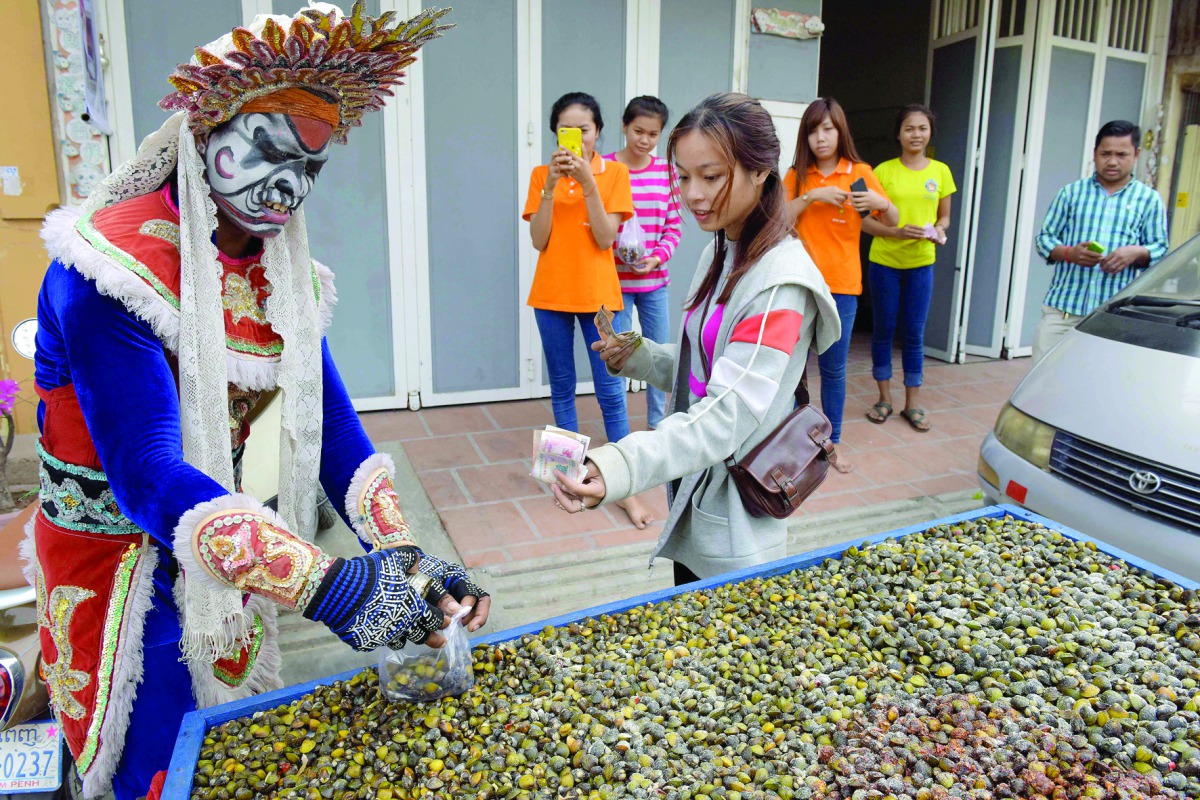 A customer buys a packet of dried river shells from Mak Sobin (L) in Phnom Penh on January 14, 2017. Mak Sobin, 25, who has been selling dried river shells as a snack for seven years, started wearing the opera costume 1.5 months ago as an attempt to attra