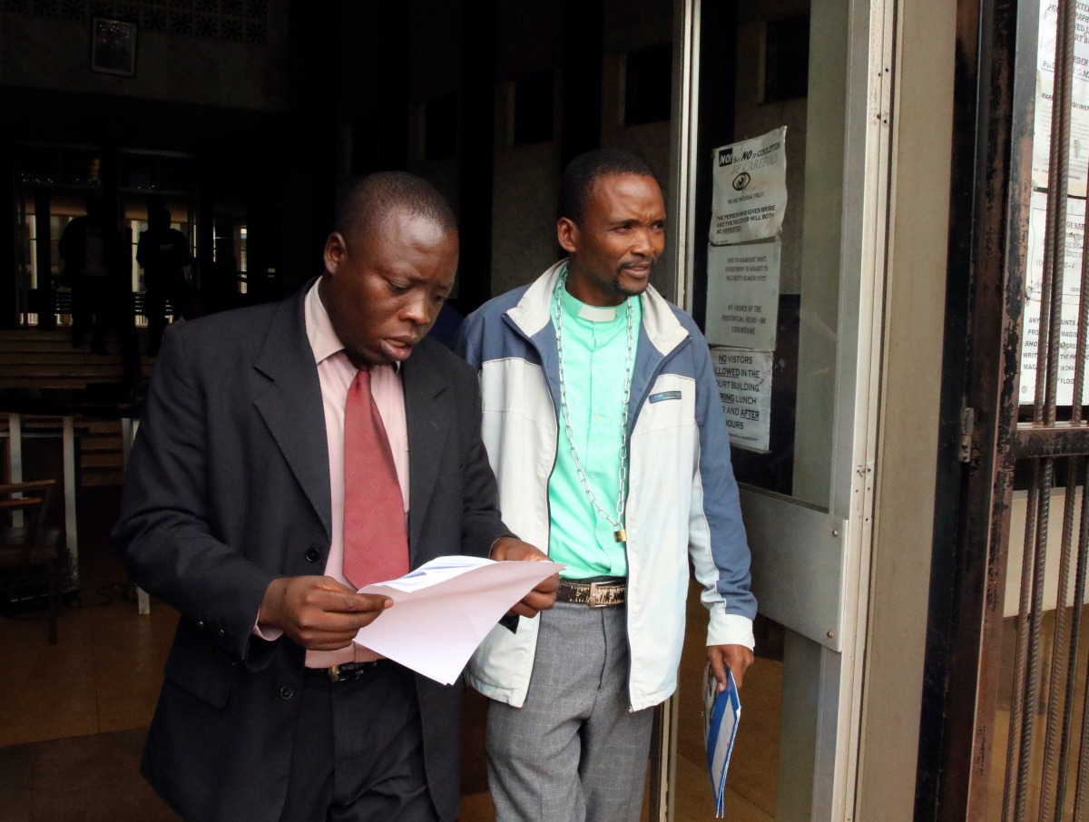 Zimbabwean Pastor Phillip Patrick Mugadza (R) is escorted by detectives at the Harare Magistrates court, where he faces charges of insulting President Robert Mugabe for allegedly prophesing the statesman would die on October 17 this year, according to the