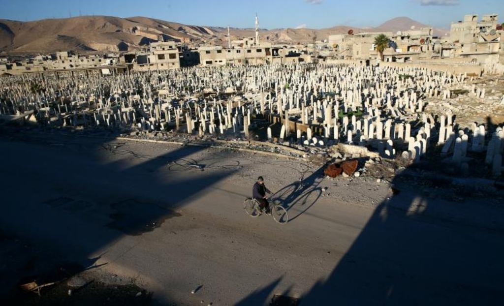 A civilian rides a bicycle past a cemetery in the rebel held besieged Douma neighbourhood of Damascus, Syria January 3, 2017. REUTERS/Bassam Khabieh