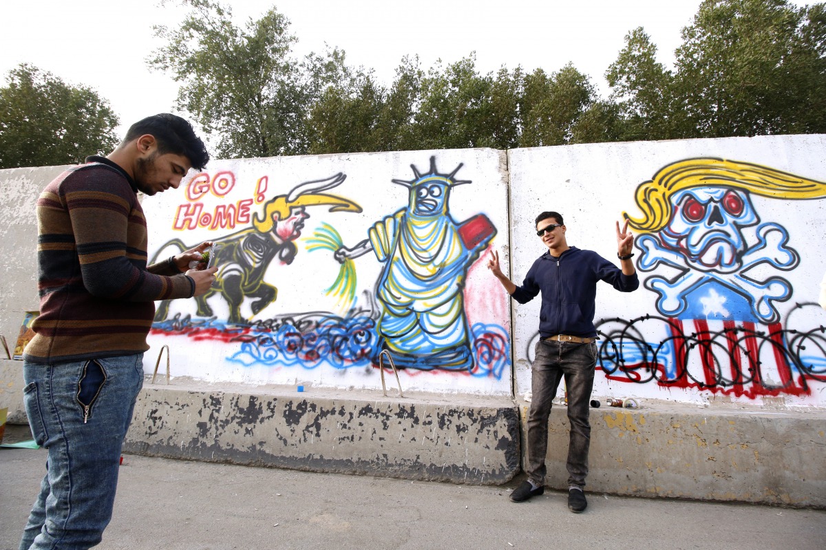 Iraqi men take pictures next to a mural featuring anti-US President Donald Trump slogans, in Basra, southeast of Baghdad, Iraq February 2, 2017. Picture taken February 2, 2017. REUTERS/Essam Al-Sudani