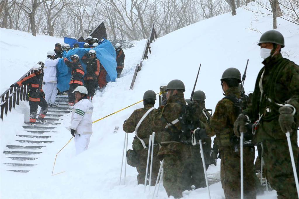 Firefighters carry a survivor they rescued from the site of an avalanche. JIJI PRESS / AFP.