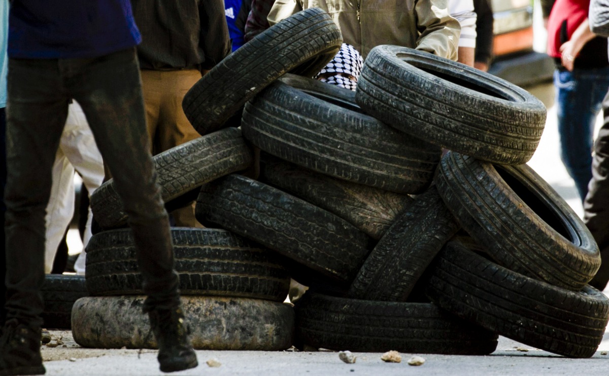 A Palestinian protestor takes cover behind a pile of tires during clashes with Israeli security forces following a weekly demonstration against the expropriation of Palestinian land by Israel in the village of Kfar Qaddum, near Nablus, in the occupied Wes