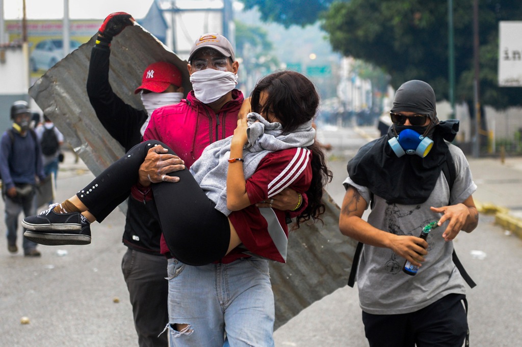 A young woman who was overcome by tear gas shot by tiot police is carried away by fellow demonstrators when opposition activists clashed with riot police in Caracas on April 10, 2017.  AFP / FEDERICO PARRA
