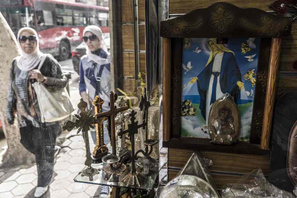 Egyptian women pass by the window of a Coptic Orthodox Churches outside a Christian church-paraphernalia shop displaying crucifixes and icons in the capital Cairo's northern suburb of Shubra, on April 11, 2017.  AFP / KHALED DESOUKI
