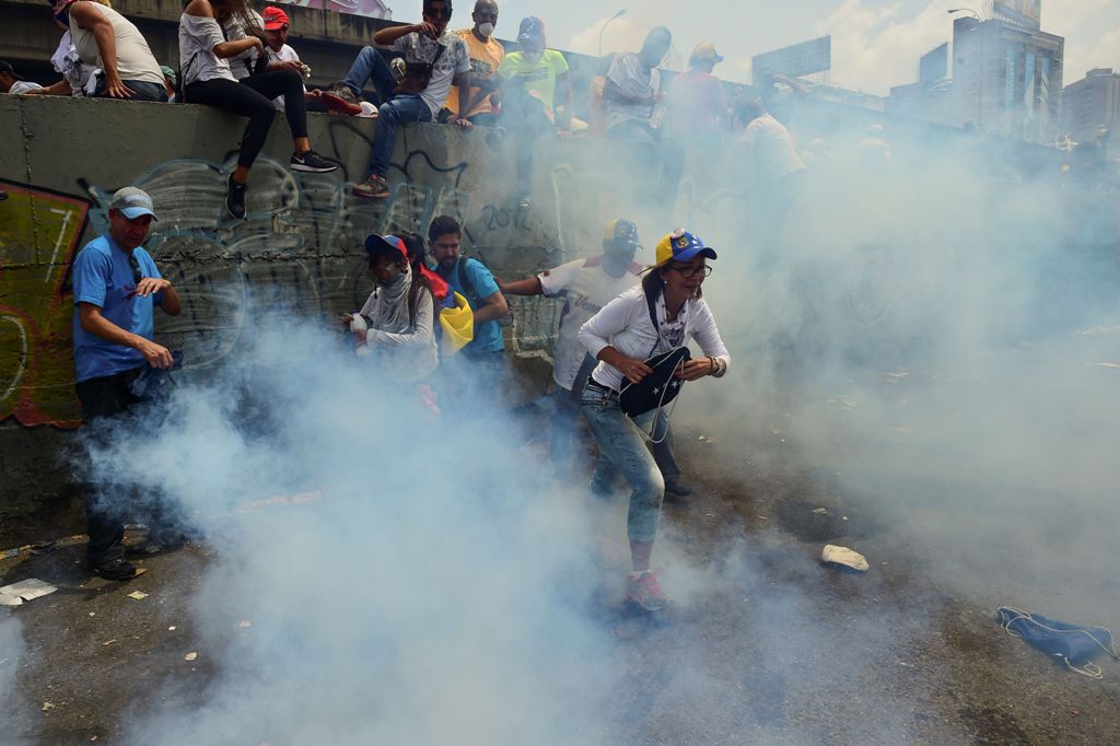 Demonstrators run away from tear gas canisters thrown by the police during a rally against Venezuelan President Nicolas Maduro, in Caracas on April 19, 2017. / AFP.