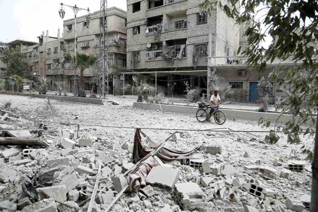 A Syrian man walks with a bicycle along a road that was destroyed in an air strike in the rebel-controlled town of Hamouria, in the eastern Ghouta region on the outskirts of the capital Damascus on May 1, 2017. / AFP / ABDULMONAM EASSA
