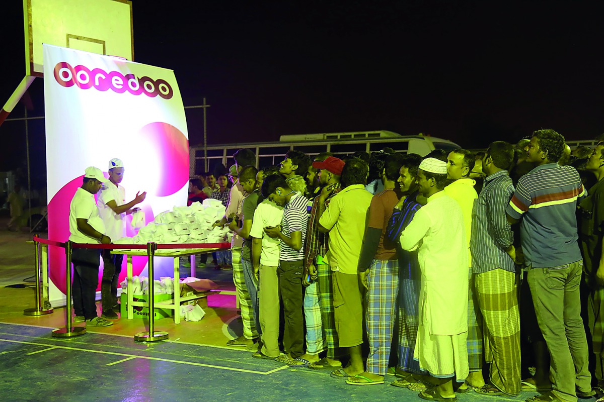 Representatives of Ooredoo distributing healthy snacks and food vouchers at a workers' camp. 
