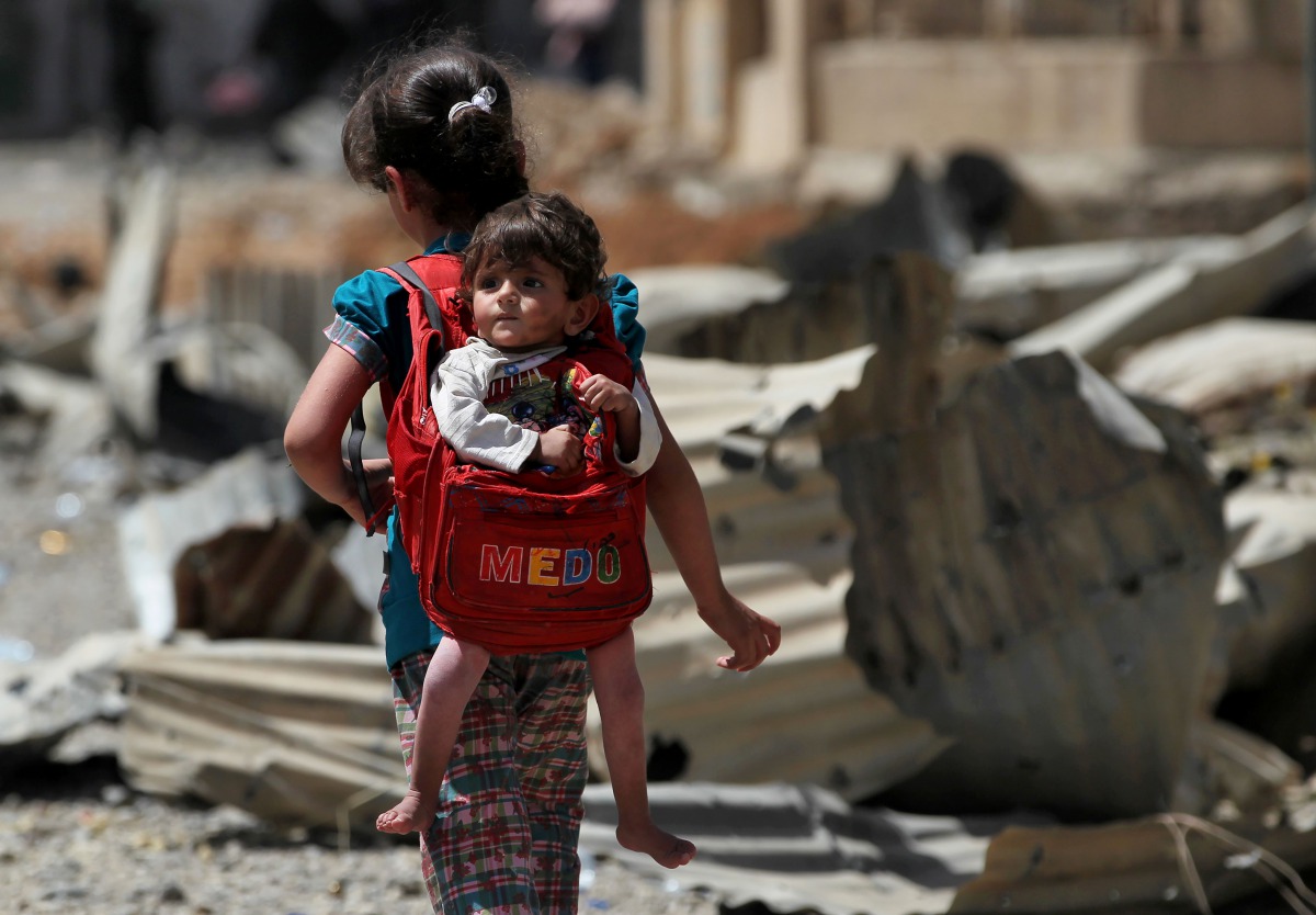 An Iraqi girl carries a baby in a backpack turned into a baby carrier as displaced Iraqis from western Mosul's al-Islah al-Zaraye neighbourhood flee their area on May 12, 2017 during a government forces' military offensive to retake the area from Islamic 