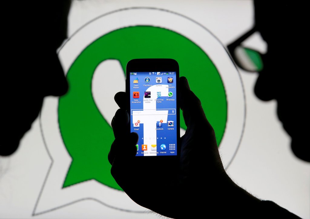 An illustration photo shows a man holding a smart phone with a Facebook logo as its screen wallpaper in front of a WhatsApp messenger logo February 20, 2014. REUTERS/Dado Ruvic /Illustration/File Photo