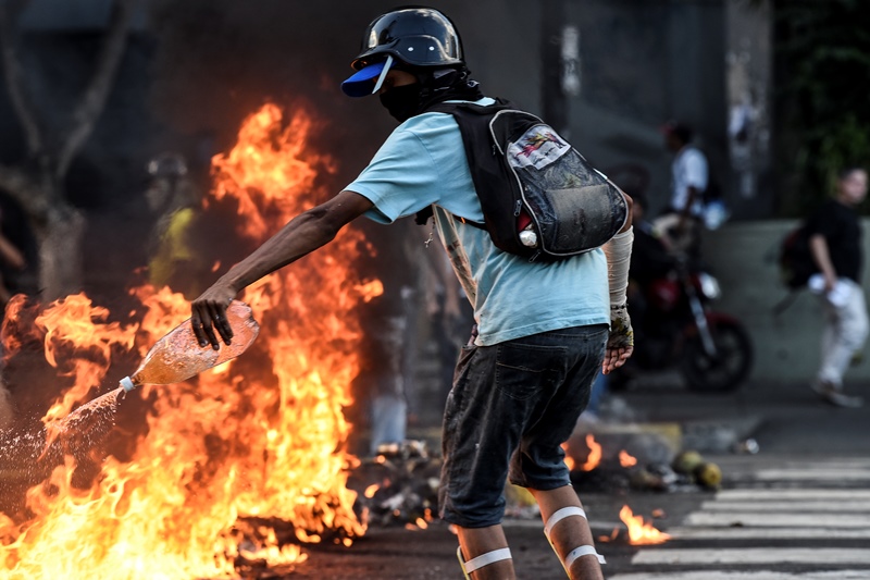 A hooded protester throws gas into the flames during a protest against the government of President Nicolas Maduro in Caracas on May 20, 2017. ( Carlos Becerra - Anadolu Agency )