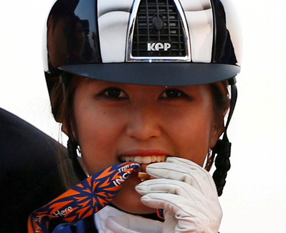 FILE PHOTO: South Korea's Chung Yoo-ra, then known as Chung Yoo-yeon, bites her gold medal as she poses after winning the equestrian Dressage Team competition at the Dream Park Equestrian Venue during the 17th Asian Games in Incheon September 20, 2014. RE