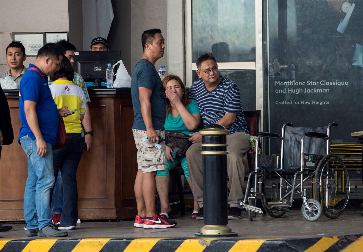 Relatives of a victim sit in front of the Resorts World Hotel following an assault in Manila on June 2, 2017. Thirty-four bodies were found in a casino complex after a gunman started a fire in the building, the local police chief said. (AFP / NOEL CELIS)