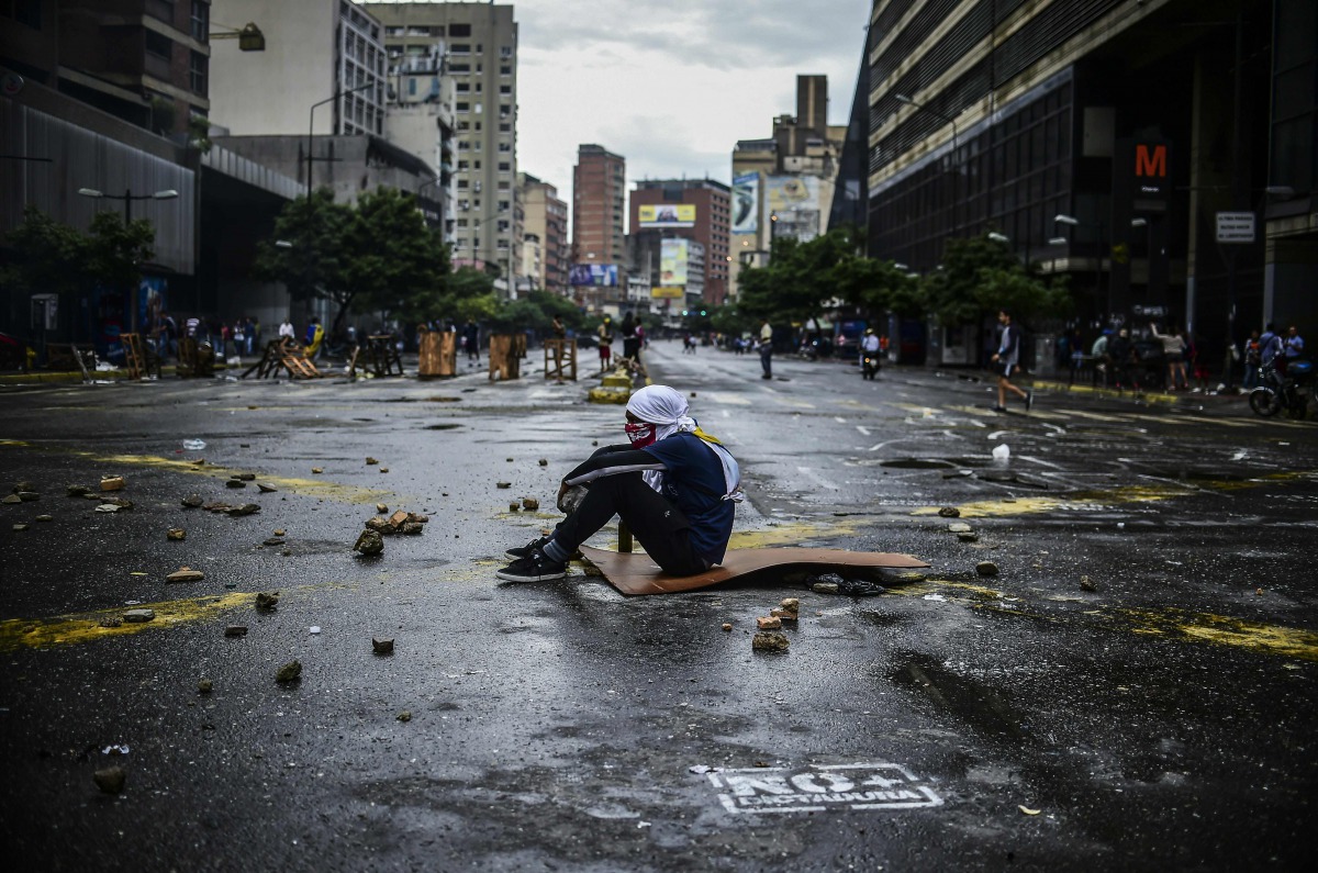 An masked opposition activist sits on the floor during a blockade to protest against Venezuelan President Nicolas Maduro in Caracas, on July 19, 2017. Venezuela's military chiefs reaffirmed their loyalty to President Nicolas Maduro on Wednesday by saying 