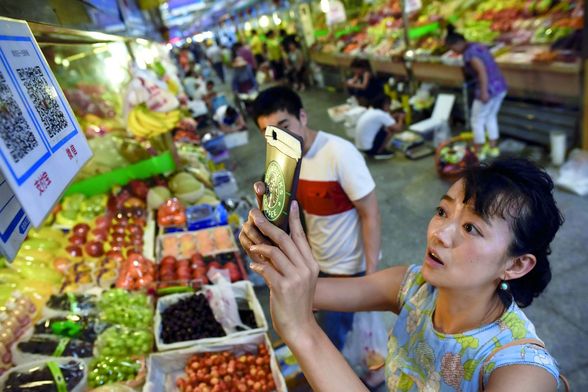  A woman making purchases by scanning QR codes using her smartphone at a fruit stall in a market in Beijing