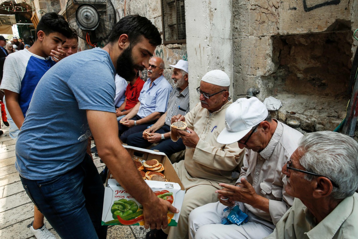 A Palestinian distributes pastries donated to support demonstrators who have kept vigil for over a week as they pray outside Al-Aqsa mosque compound in the old city of Jerusalem on July 26, 2017. AFP / Ahmad Gharabli