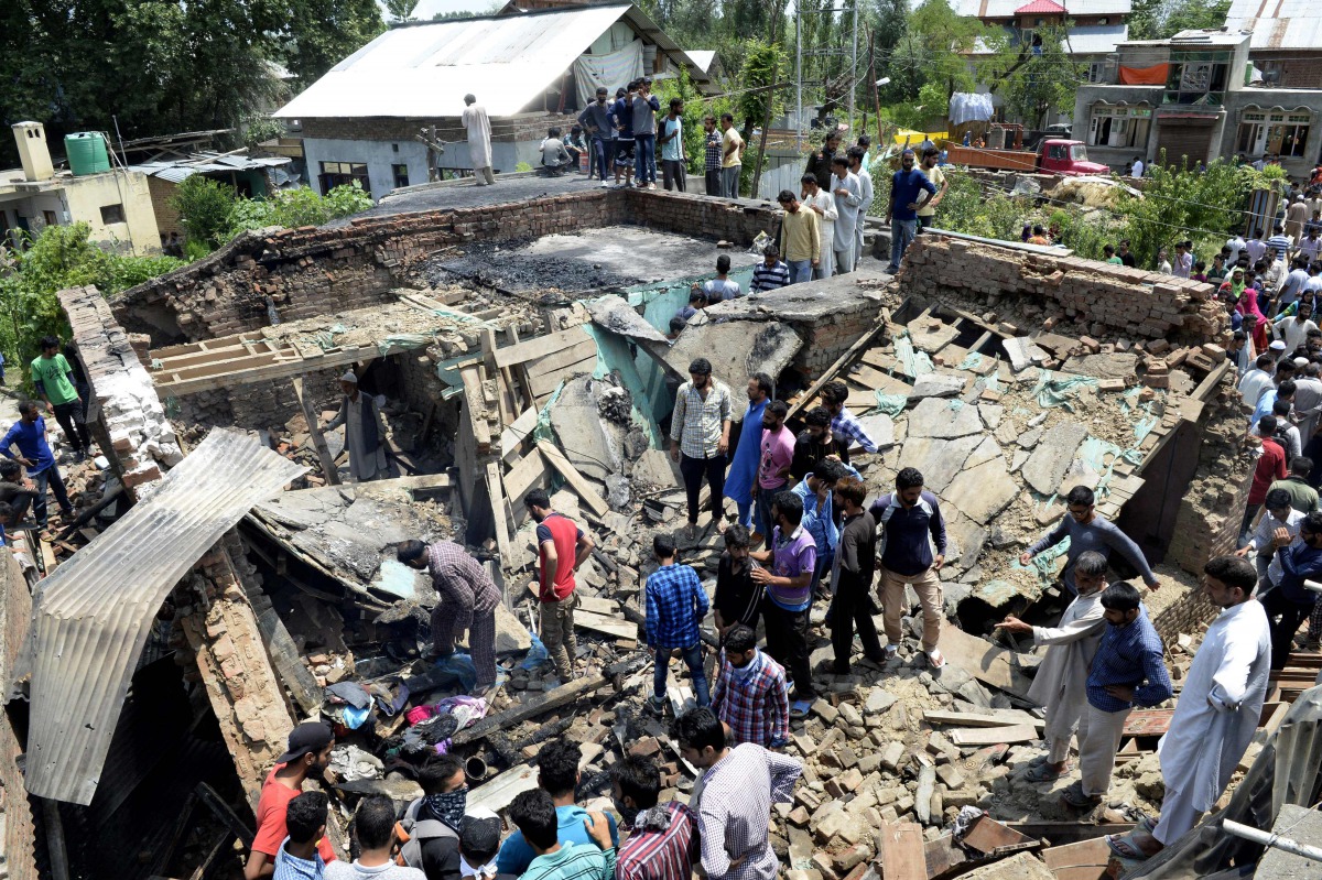 Kashmiri villagers walk through a damaged house where two suspected rebels were killed during a gunfight with government forces in the Hakripora village of Pulwama on August 1, 2017. (AFP / TAUSEEF MUSTAFA)
