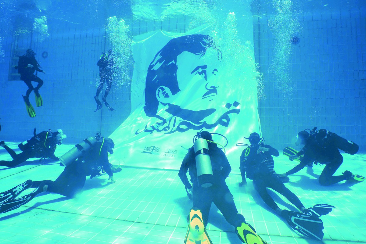 Divers instal Tamim Al Majd billboard underwater at the Aquatic Center of Qatar University Sports Activities Department.