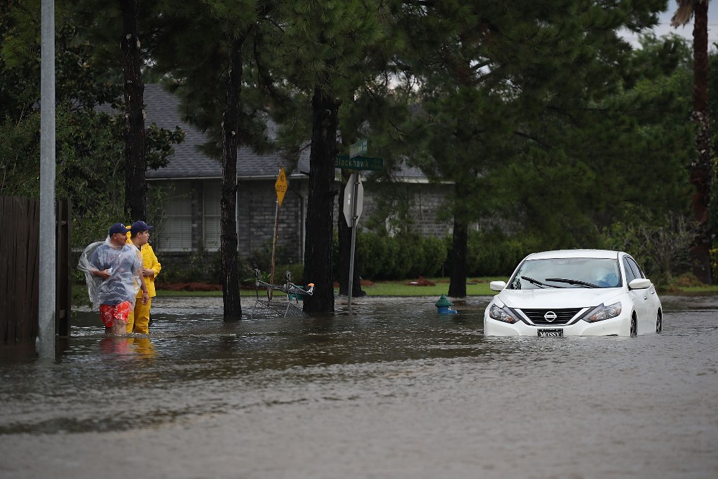 People walk past an abandoned car after the area was inundated with flooding from Hurricane Harvey on August 29, 2017 in Houston, Texas. / AFP.